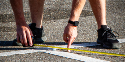 Nahaufnahme von Parkplatz mit Händen die auf ein Maßband zeigen.