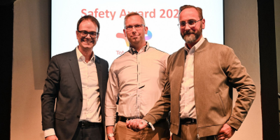 Drei Männer posieren bei einer Veranstaltung mit einem Award auf der Bühne - Blick in die Kamera