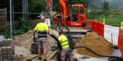 2 Bauarbeiter beim Tiefbau mit Bagger bei der Leitungsverlegung.